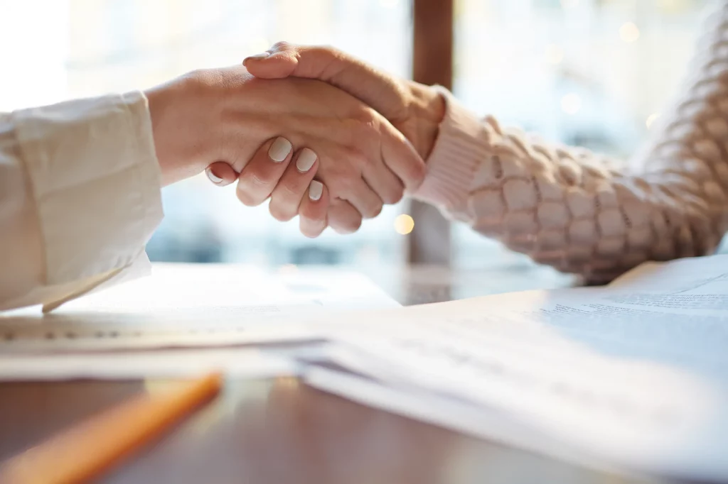 Handshake over documents, symbolizing partnership and funding agreements.