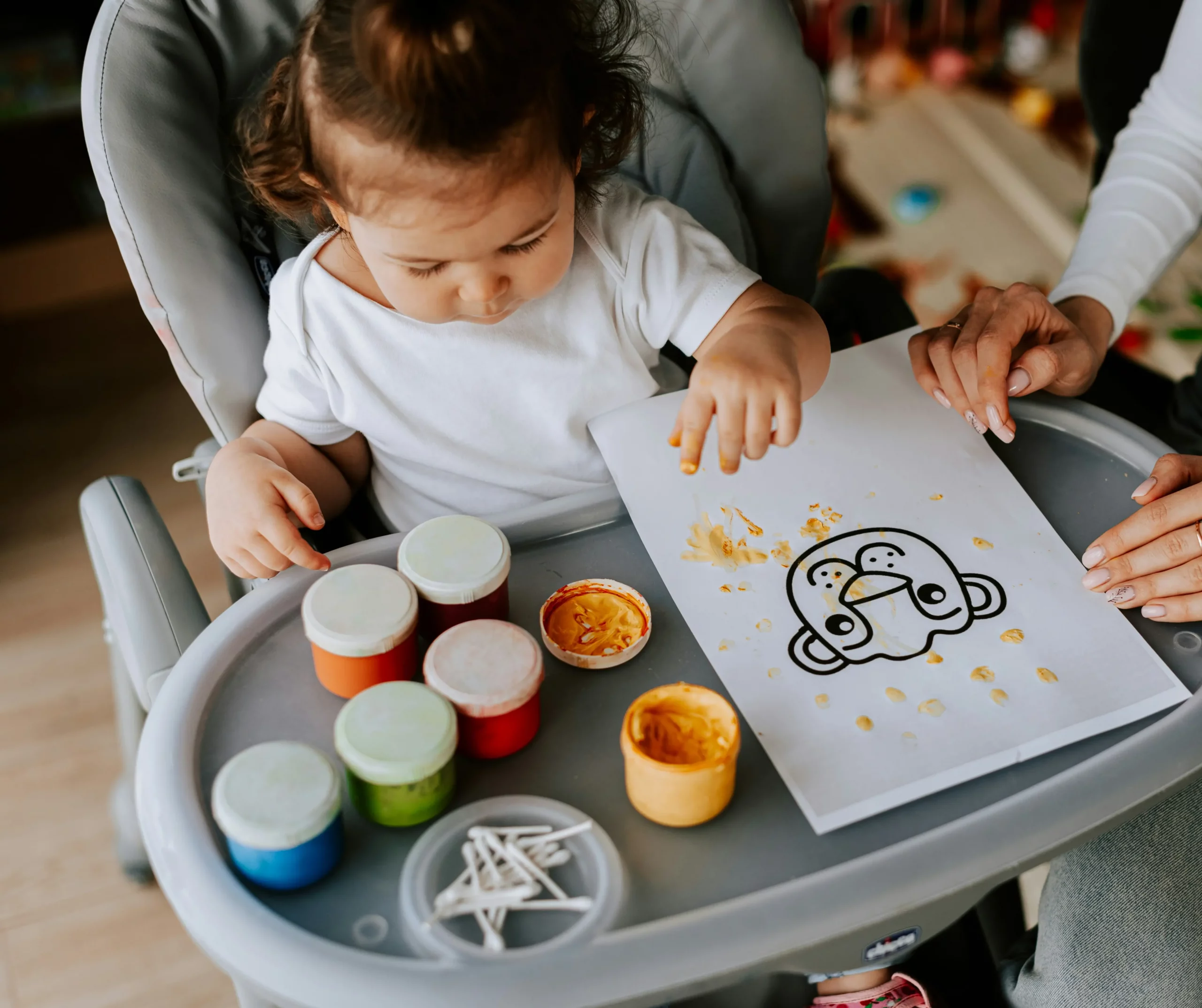 Toddler finger painting a duck picture with bright colors. AED service.