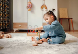 Toddler playing with wooden stacking toy on rug. Early childhood development.