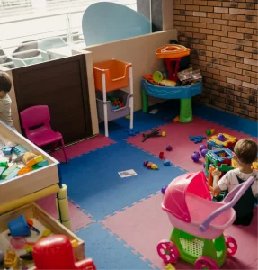 Colorful playroom with children playing with blocks, toys, and a pink stroller on pink and blue mats.