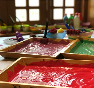 Paint-filled trays in red, maroon, and green, ready for art projects.