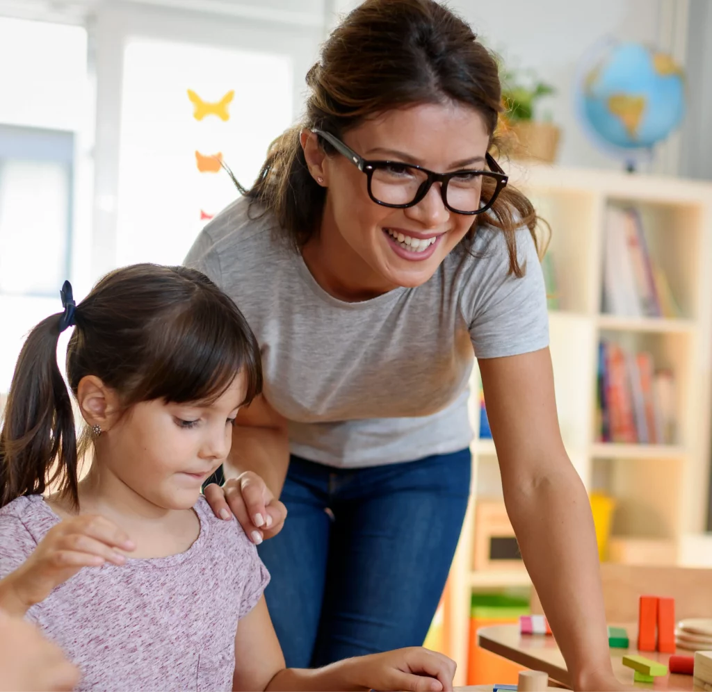 Teacher helping a young girl with blocks in a classroom, supporting our association.
