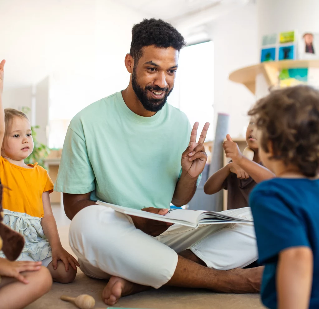 Man reading to children in an association setting, holding up two fingers.