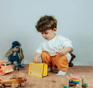 Child playing with a yellow toy radio and other toys on a wooden floor.